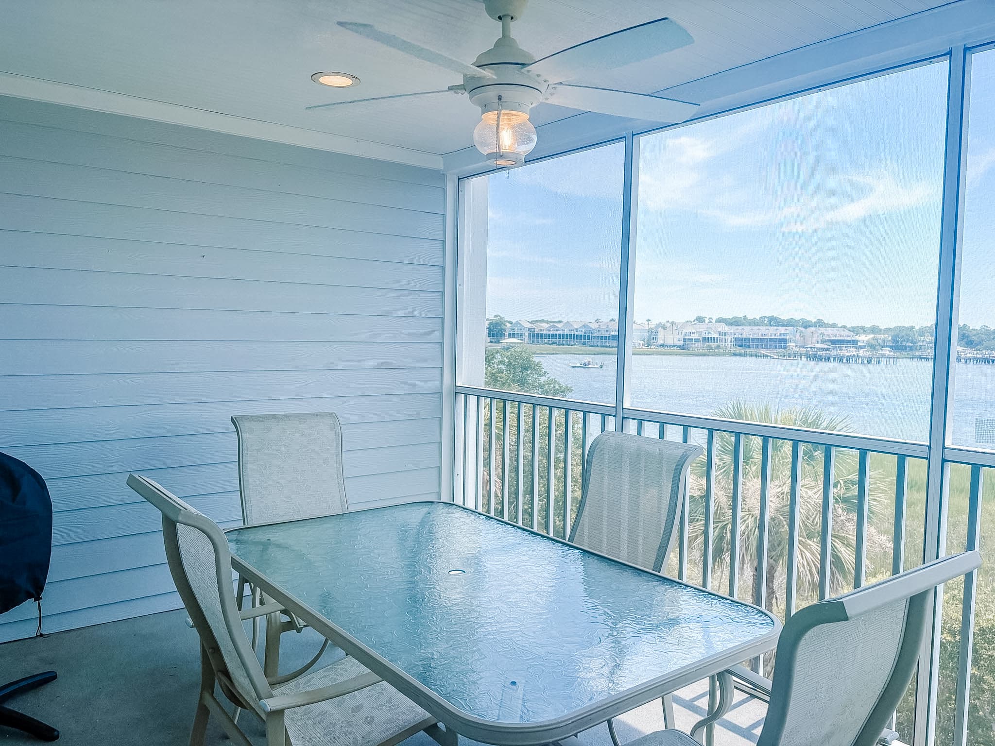 Screened-in porch with a glass table and chairs overlooking a bright, sunny coastal waterway.