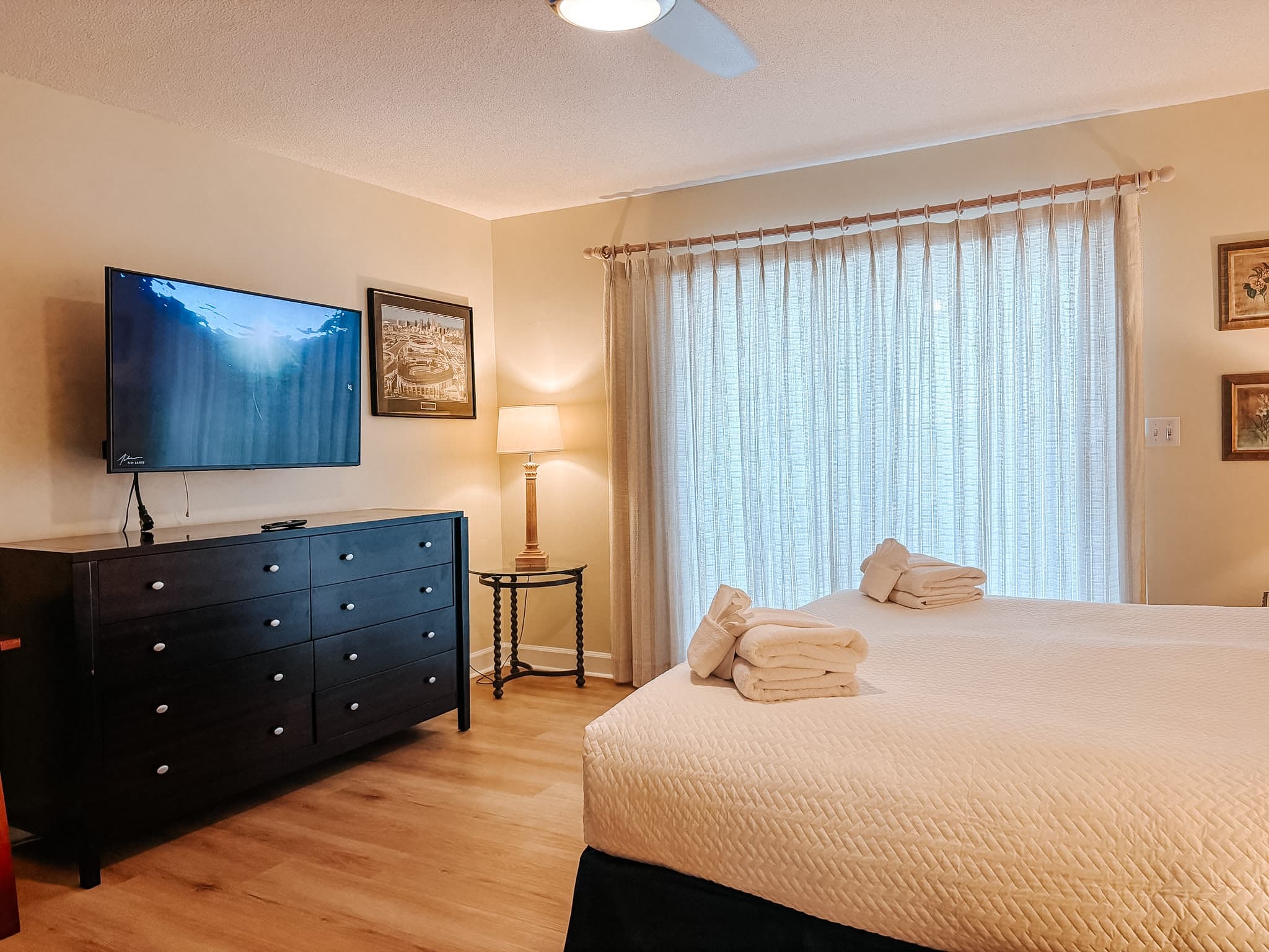 Bedroom with a black dresser, wall-mounted TV, and a bed with white folded towels.
